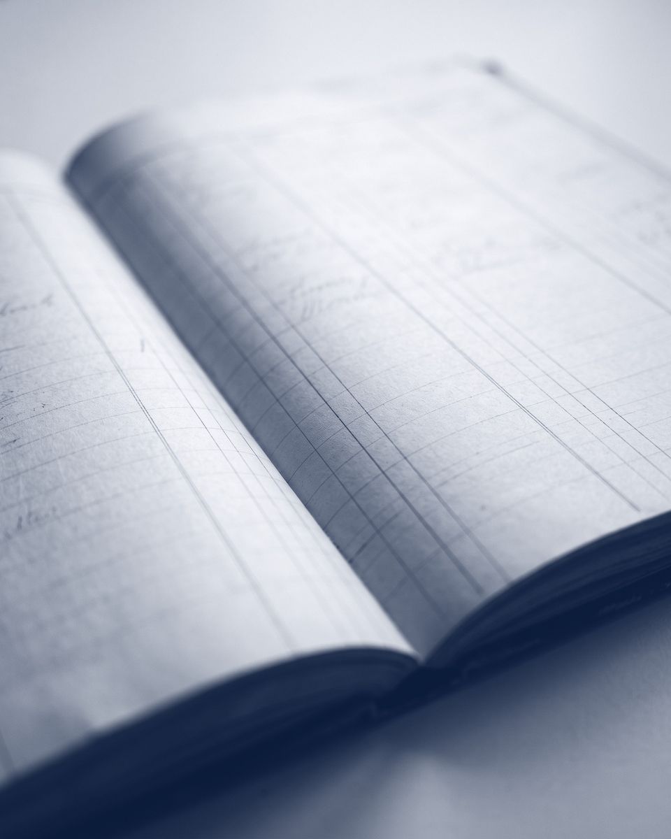 An open ledger book with ruled columns, photographed at a low angle in deep ink blue.