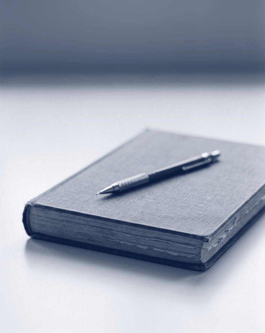 A closed cloth-bound notebook with a mechanical pencil on its cover, in deep ink blue.